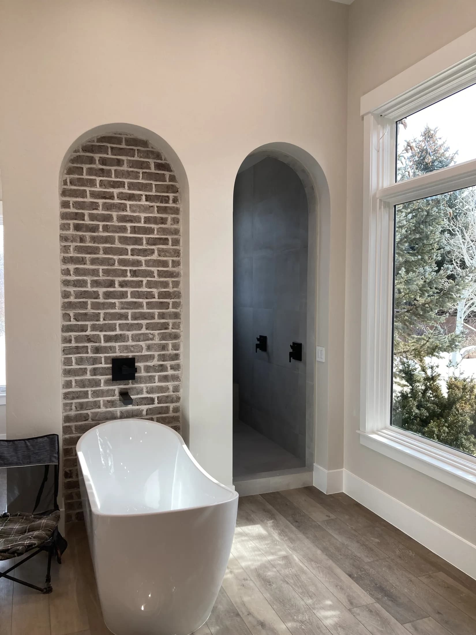 Freestanding bathtub framed by arched brickwork and tall windows.