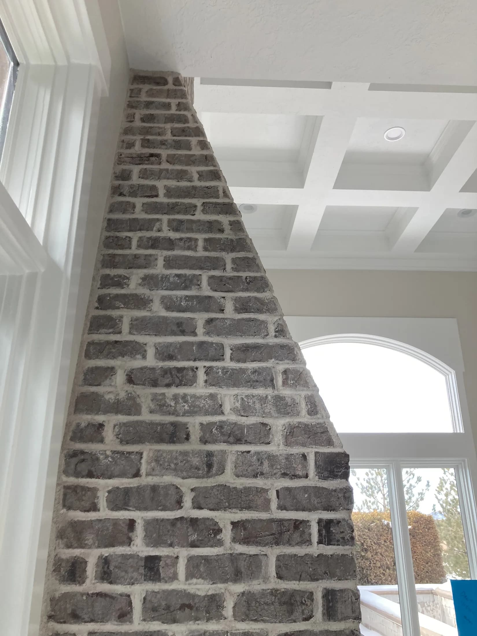 Gray brick chimney rising beside tall windows and a coffered ceiling.