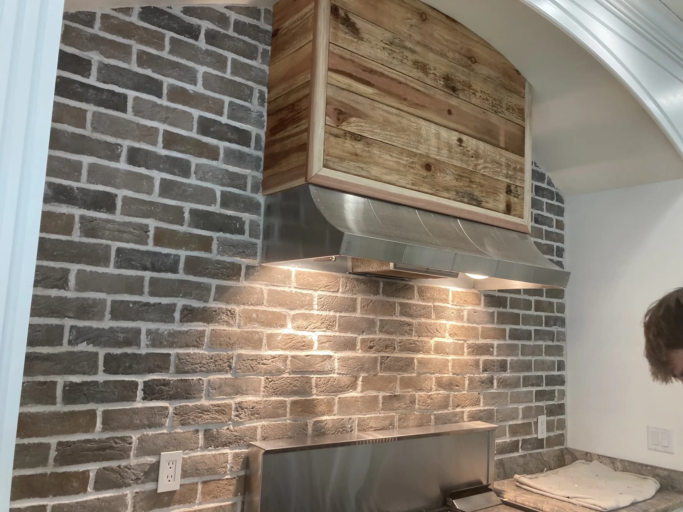Gray brick backsplash surrounding a custom wood and stainless range hood.