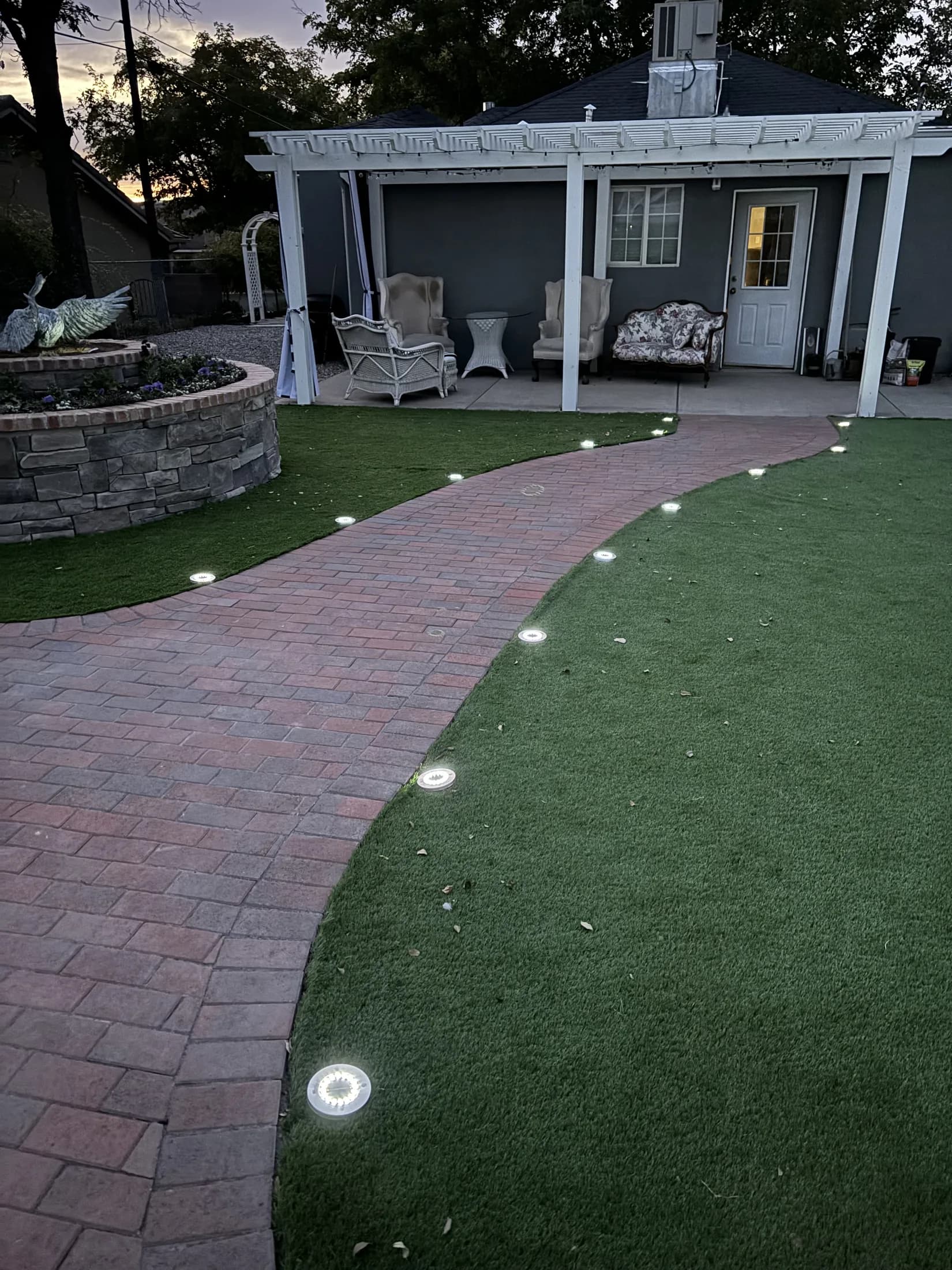 Curving brick-paver walkway with inset lighting, turf, and a pergola.