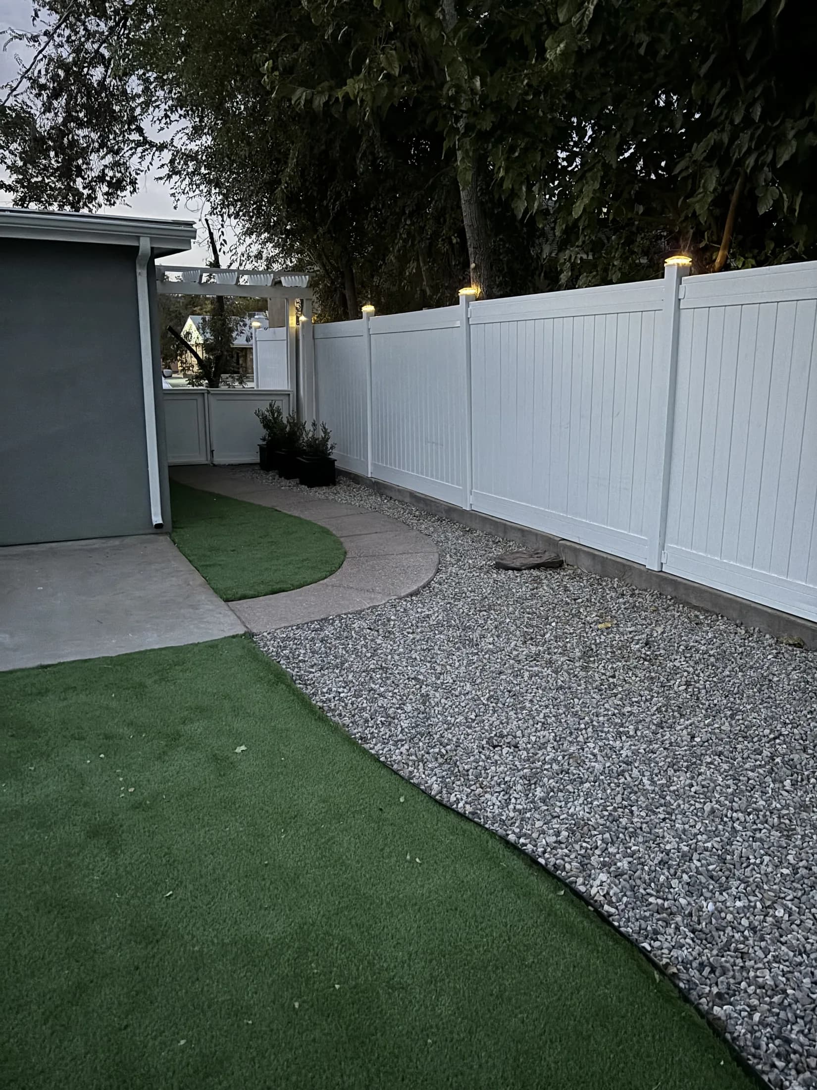 Finished artificial-turf yard with gravel path and white privacy fence.
