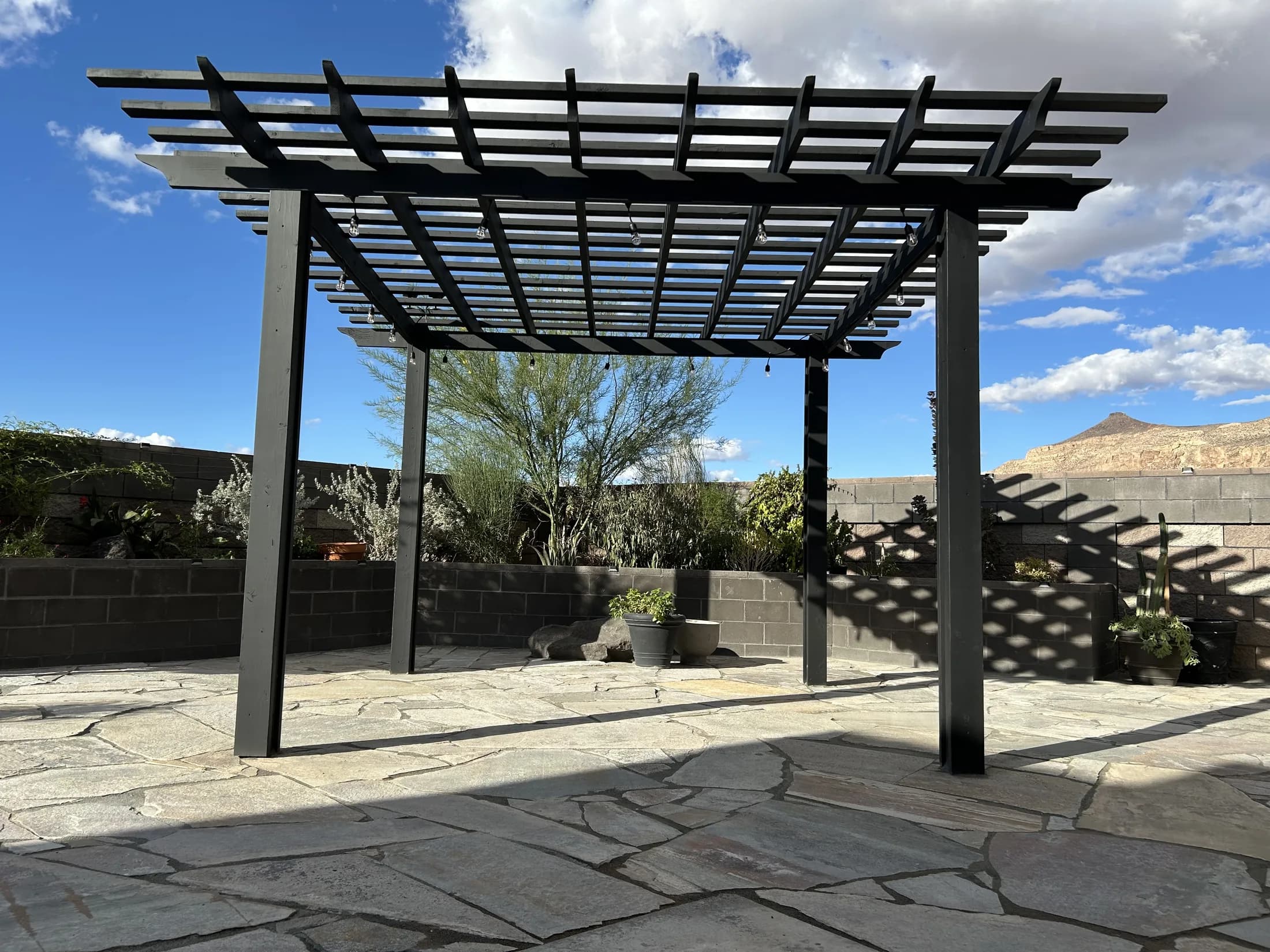 Black pergola over a flagstone patio with desert mountain views.