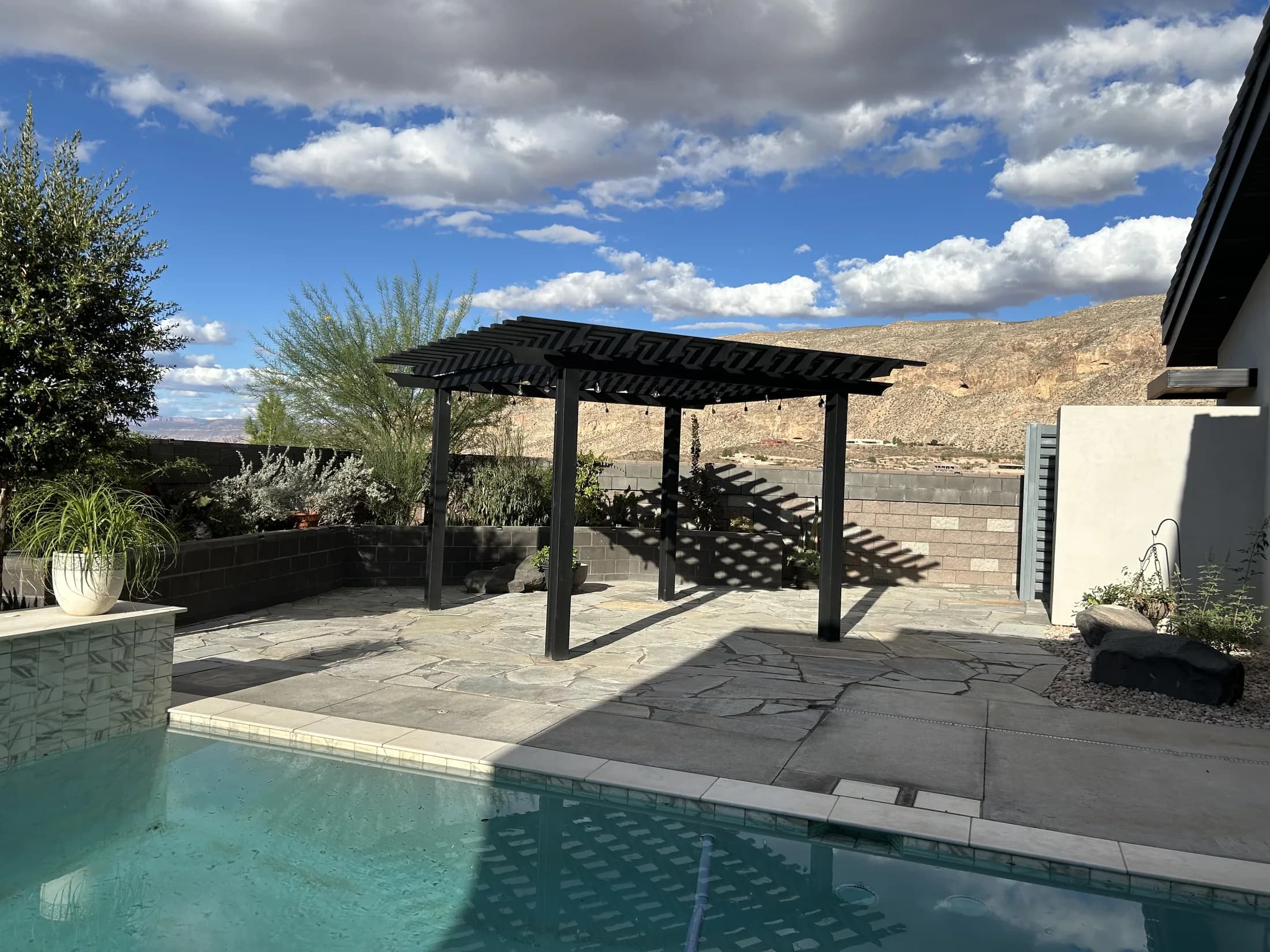 Black pergola and flagstone patio beside a desert swimming pool.