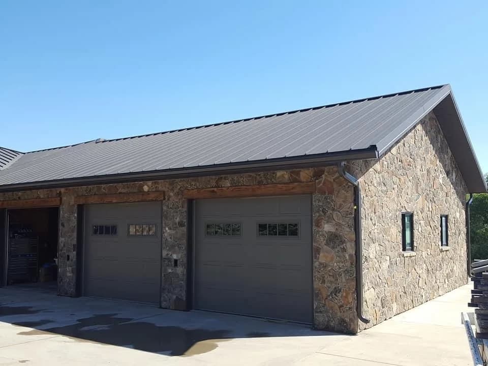 Detached garage finished in natural stone with dark overhead doors.