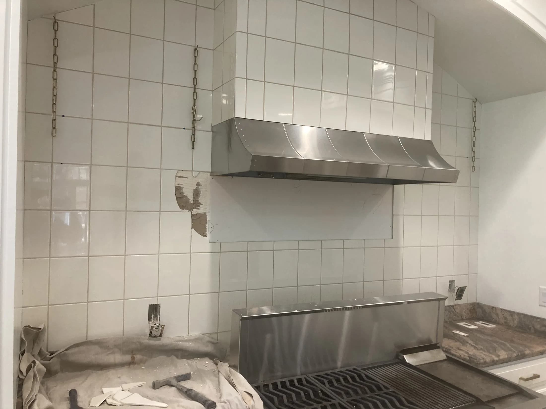 White tile backsplash and stainless range hood during kitchen installation.